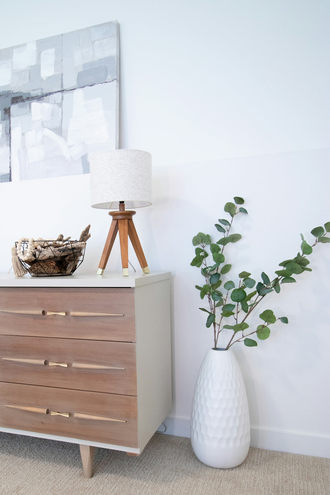 A white vase with a plant on top of it next to a dresser